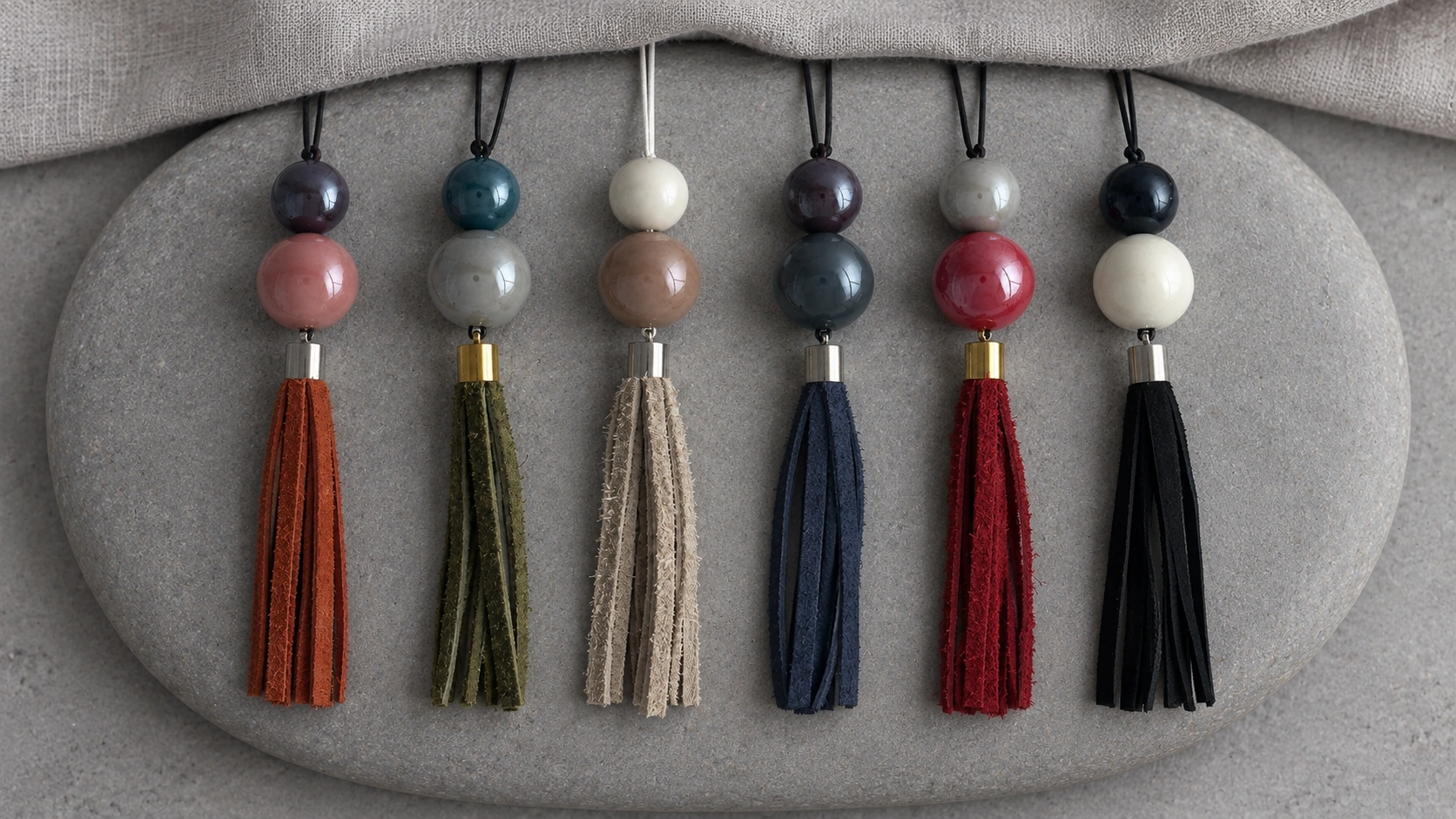 Six MOORMI ceramic and leather pendants with the neck cords continuing beneath pale linen
